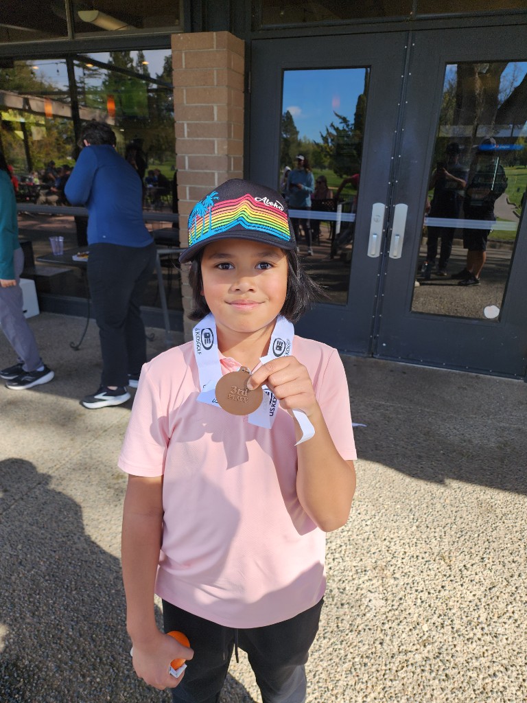 Shay holding a U.S. Kids Golf 3rd Place medal and an orange golf ball